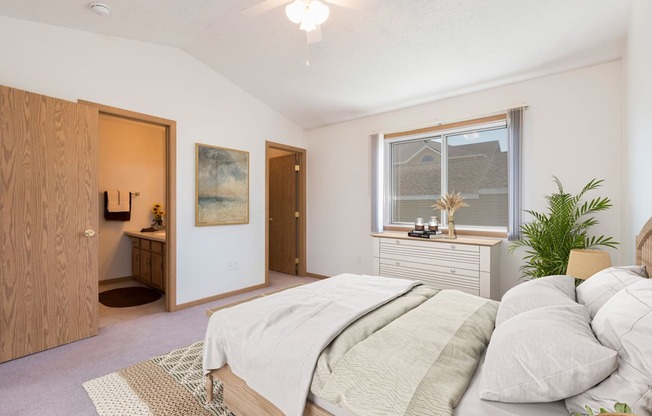 Bismarck Pebble Creek Apartments.  a bedroom with a large bed and a bathroom in the background. a large window fills the room with natural light