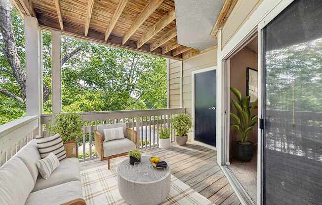 A wooden balcony with a couch, chair, and potted plants.