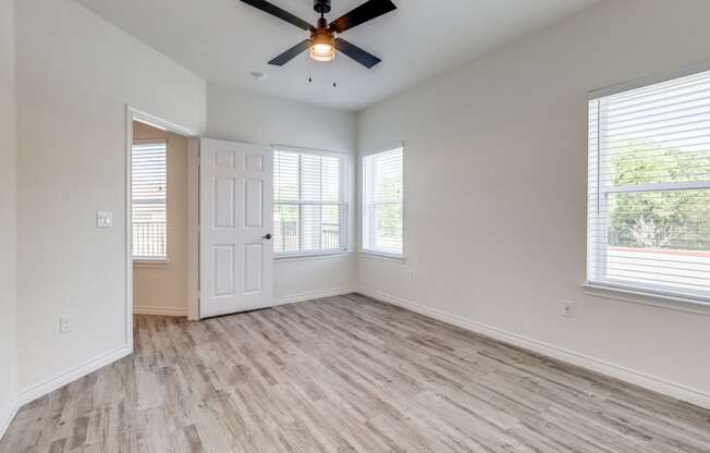 an empty living room with a ceiling fan and windows