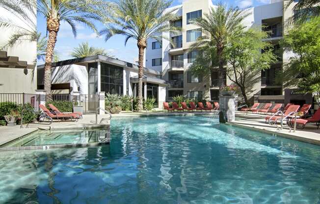 a swimming pool with chaise lounge chairs and palm trees in front of an apartment building