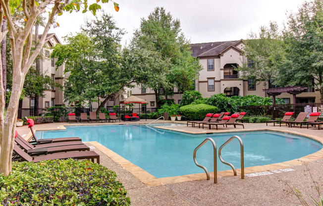 a swimming pool with chairs and trees and an apartment building in the background