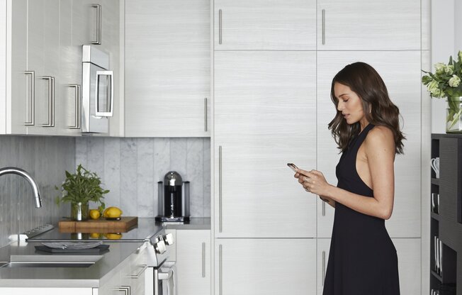 A woman in a black dress is standing in a kitchen.