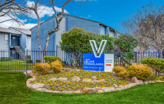 a round flower bed with yellow flowers in front of a blue building with a sign that says