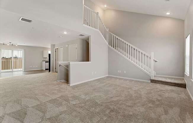 A spacious living room with a staircase and a kitchen area in the background.