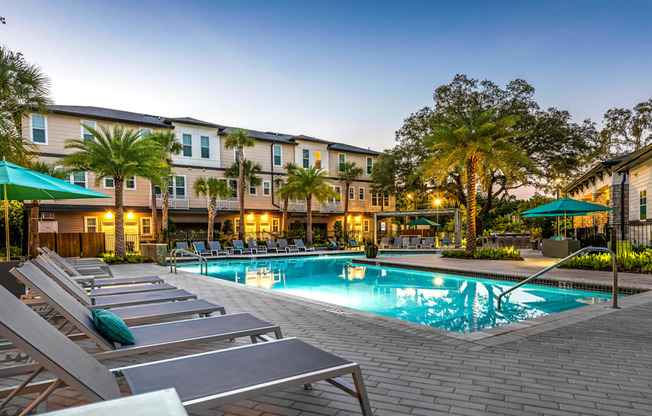 A pool surrounded by lounge chairs and umbrellas in front of a building.
