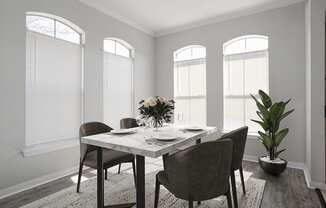 a dining room with windows and a table with a vase of flowers on top of it