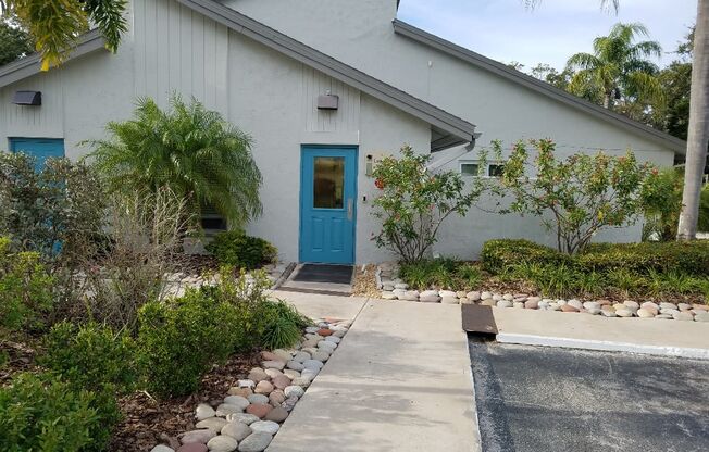 a white building with a blue door and a walkway with plants and trees