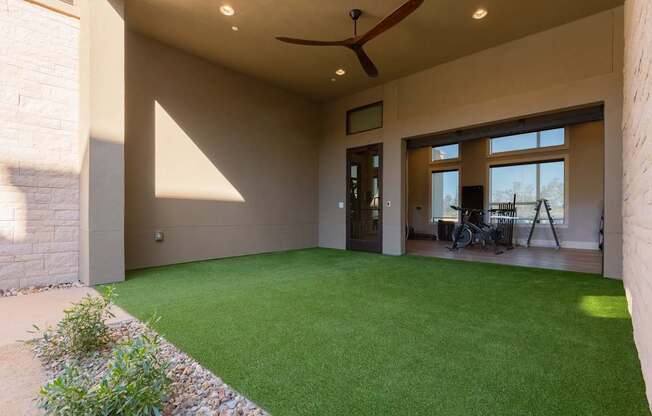 A patio with a green lawn and a ceiling fan.
