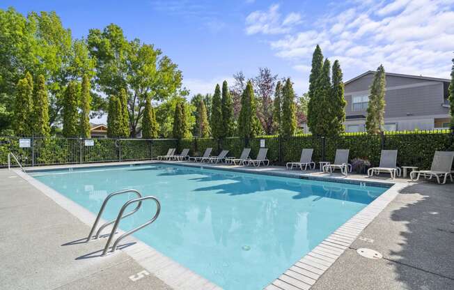 a swimming pool with lounge chairs and trees in the background