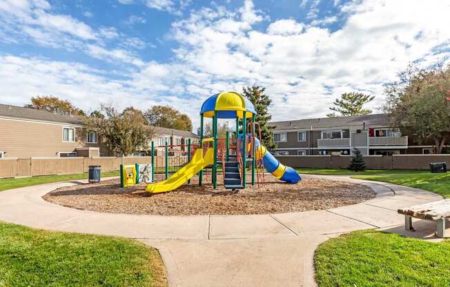 A playground with a yellow and blue slide in the middle of a grassy area.
