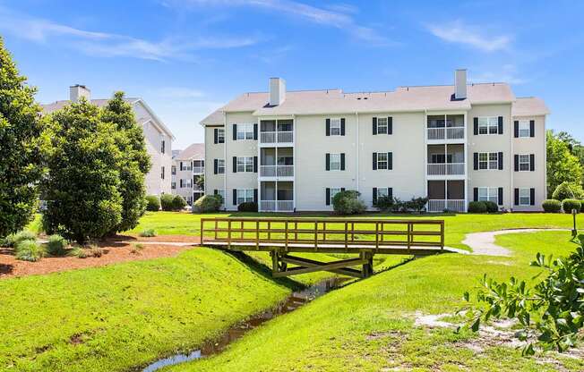 A white apartment building with a yellow bridge over a small stream.
