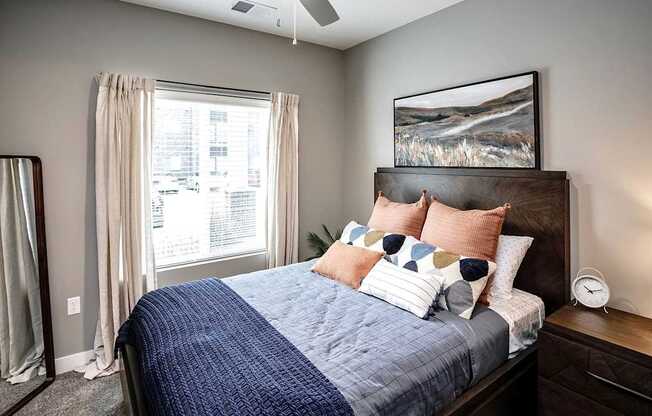 A bedroom with a bed, pillows, a ceiling fan, and a window with curtains.