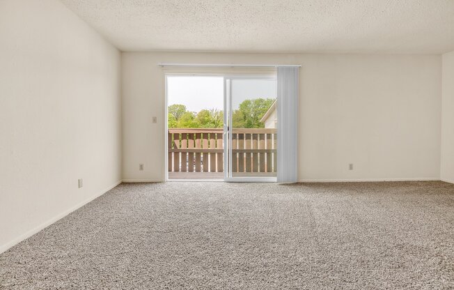 A room with a carpeted floor and a sliding glass door leading to a balcony.