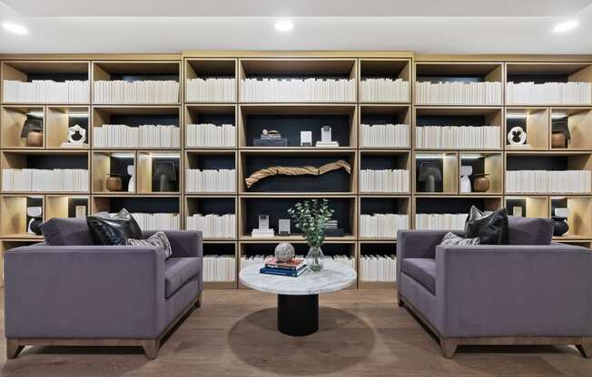 a living room with two couches and a table in front of a book shelf