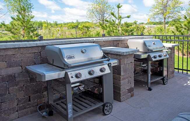 Two grills on a patio with a brick wall.