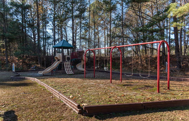 A playground with a red swing set and a green roofed structure.