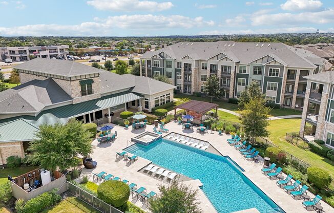 A large swimming pool surrounded by lounge chairs and umbrellas is the centerpiece of a resort-style outdoor area.
