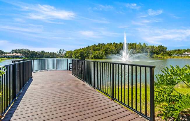 Community wooden-paneled walking path next to the pond with a view of a water fountain at Hunters Green in Tampa, Florida.