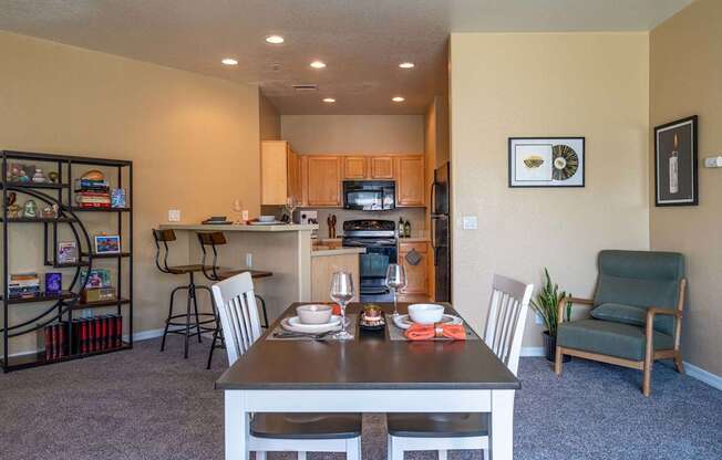 A dining room with a table set for two and a kitchen area in the background.