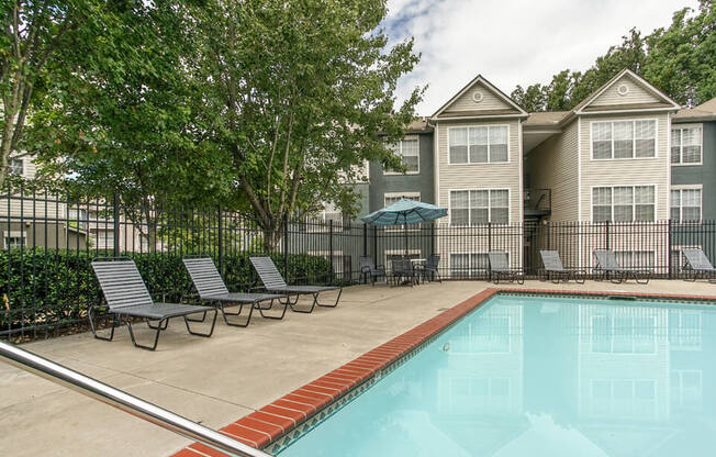 A swimming pool in front of a building with a fence and trees.