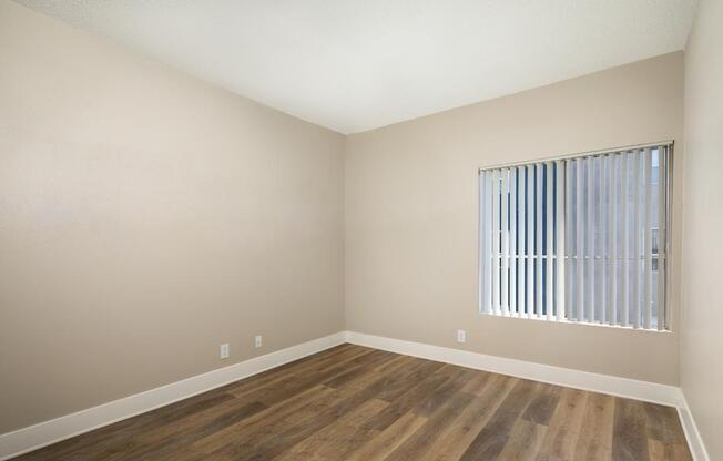 A room with wooden flooring and a window with blinds.