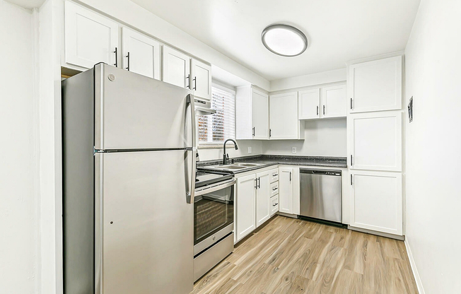 Modern kitchen with sleek stainless steel appliances, bright white cabinetry, and elegant wood flooring.