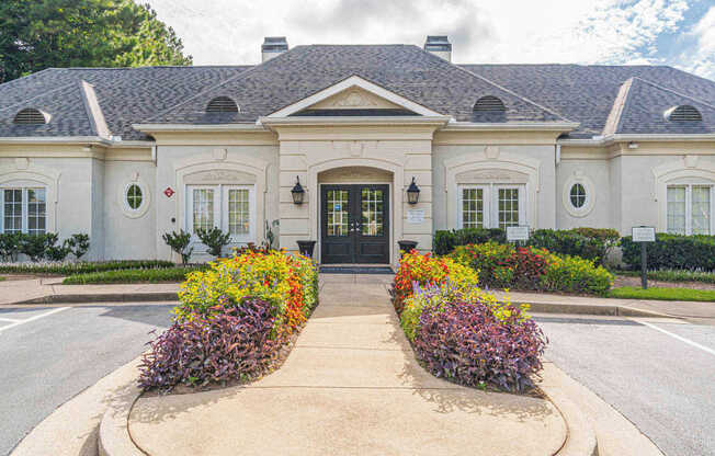 A white building with a black door and windows surrounded by flowers.