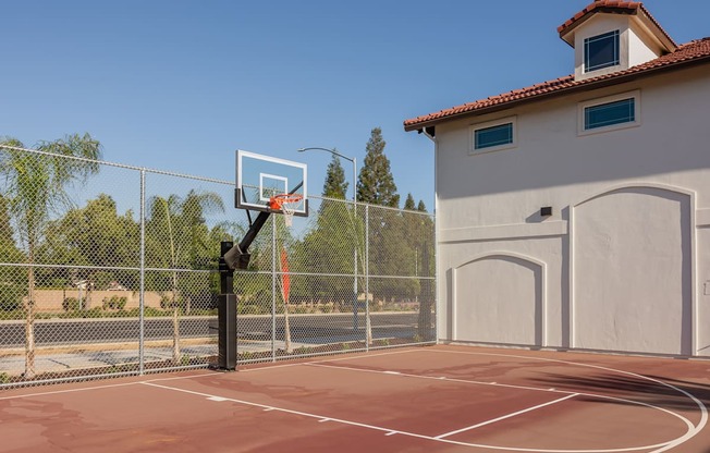 A basketball court with a hoop and a fence in front of a building.