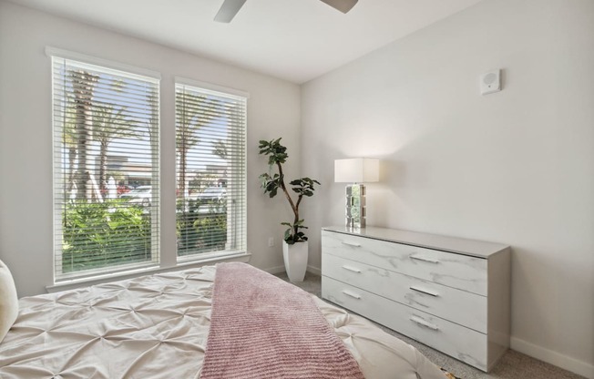 A bedroom with a bed, dresser, and window with blinds.