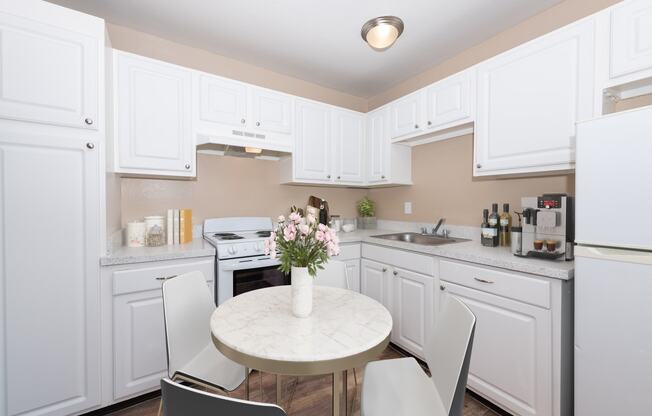 a kitchen with white cabinets and a white marble table with four white chairs