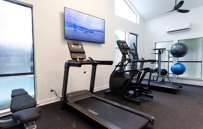 a gym with cardio equipment and a tv on the wall