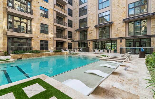 A large swimming pool in front of a building with a green lawn around it.