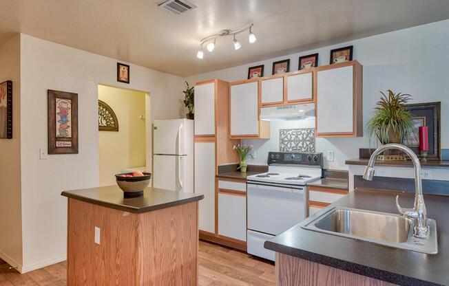 Kitchen with stainless steel sink, black countertop island, stove top with oven, plenty of cabinetry, wood floors