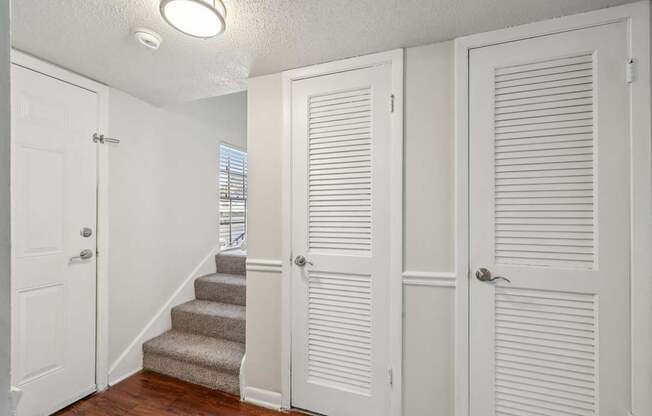 A white door is on the left of a hallway with a staircase.