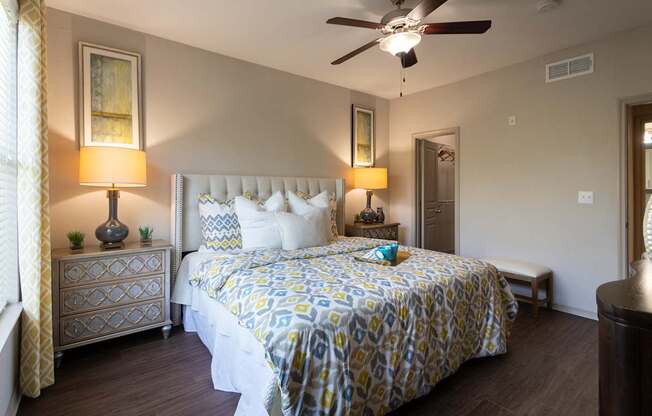 A bedroom with a bed, nightstand, and a ceiling fan in the 826 square foot 1 bedroom, 1 bathroom apartment at The Brownstones Townhome Apartments in the Far North Dallas neighborhood of Dallas, TX.