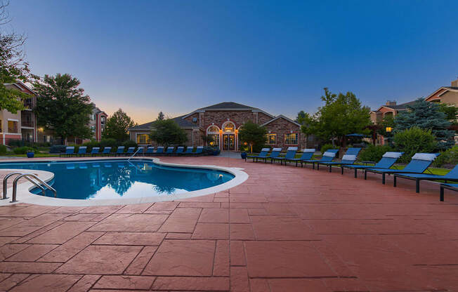 A pool surrounded by a red tile patio and lounge chairs.
