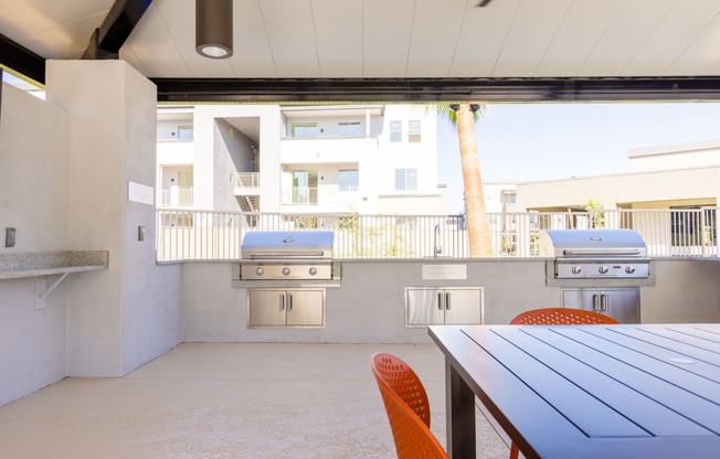 a patio with a table and chairs and two barbecue grills