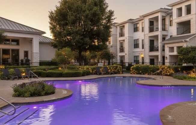 A swimming pool in front of apartment buildings at dusk.