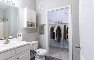 A white bathroom with a toilet, sink, and a closet with clothes.