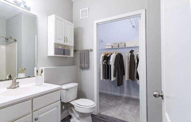 A white bathroom with a toilet, sink, and a closet with clothes.