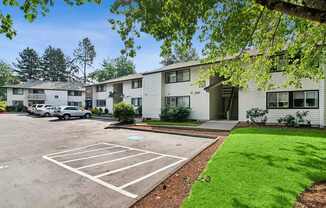A parking lot in front of a building with a green lawn.