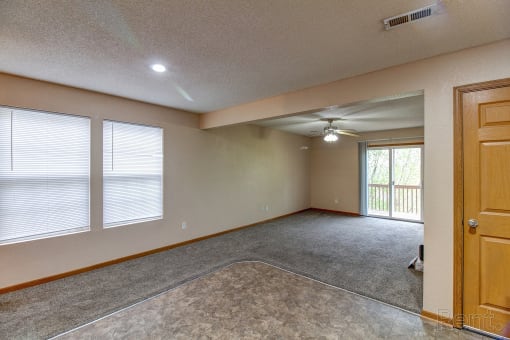 an empty living room with a ceiling fan and windows