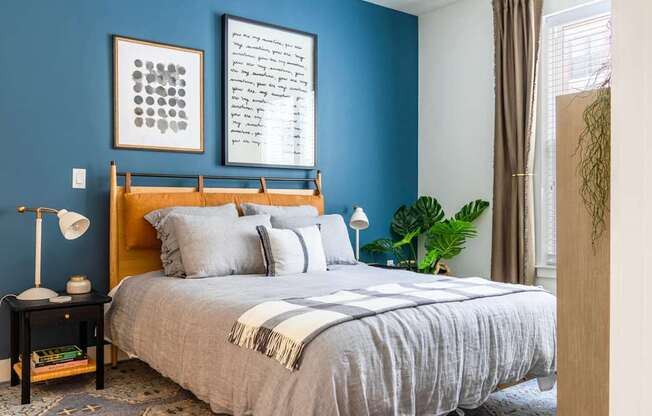 A bedroom with a bed, a nightstand with a lamp, and a framed piece of artwork on the wall.
