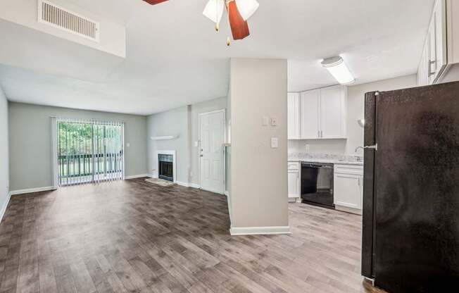 A kitchen and living area with a refrigerator, oven, and cabinets, fireplace, and glass doors leading to a balcony at Gwinnett Square Apartments in Duluth, GA