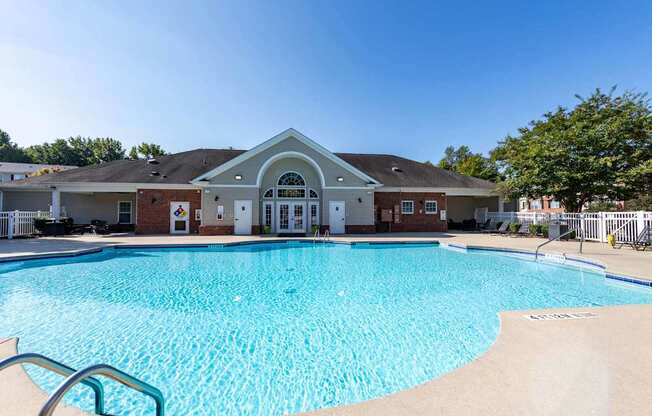 A large swimming pool in front of a building with a white fence around it.
