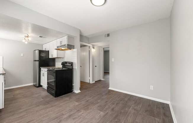 an empty living room with a kitchen with a stove and refrigerator