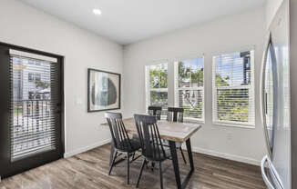 A dining room with a table and chairs and a fridge.