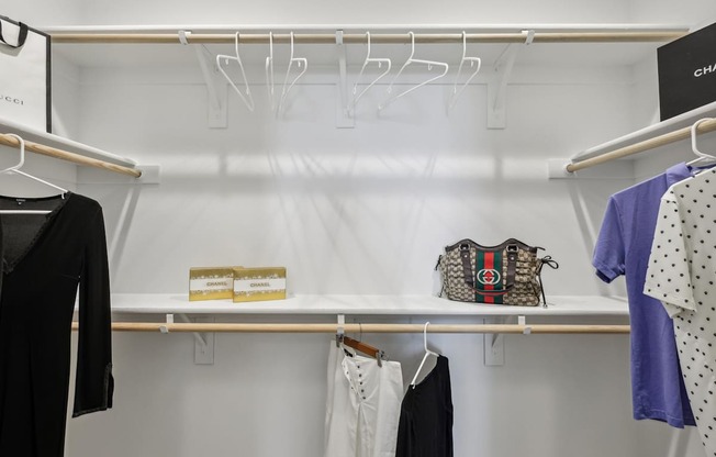 A closet with clothes hanging and a purse on the shelf.