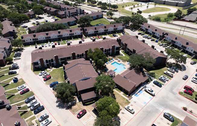 A bird's eye view of a residential area with houses, cars, and a swimming pool.