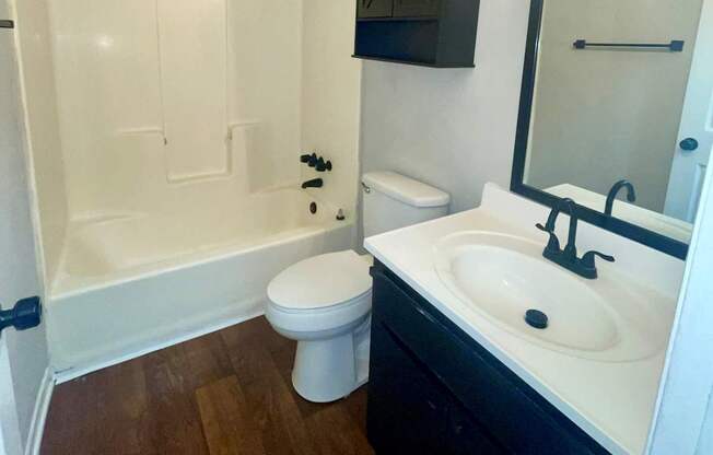 A white toilet sits in a bathroom with a black cabinet and a white sink.